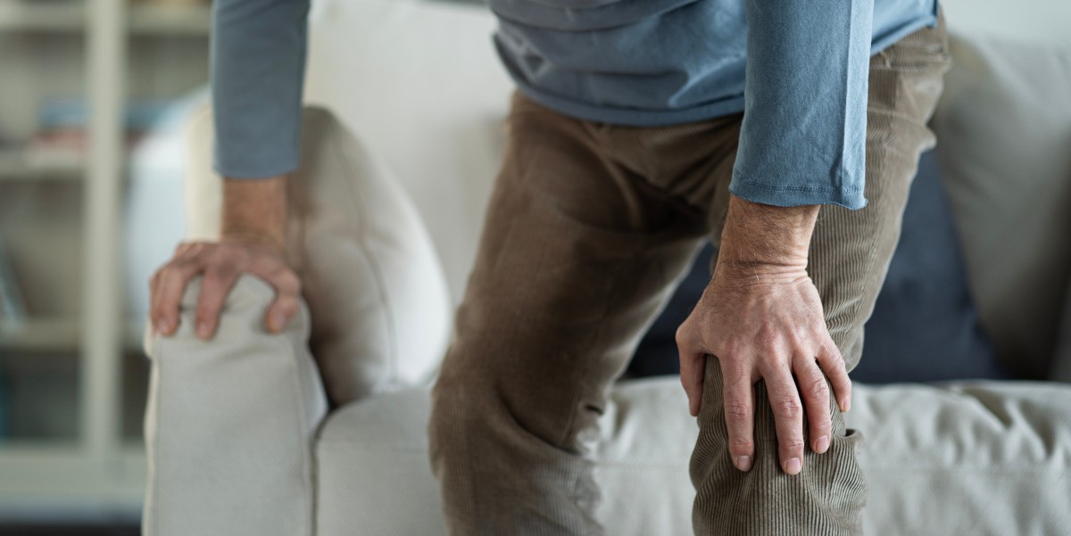 A person rising from an armchair, supporting themselves with one hand on the chair and the other on their knee