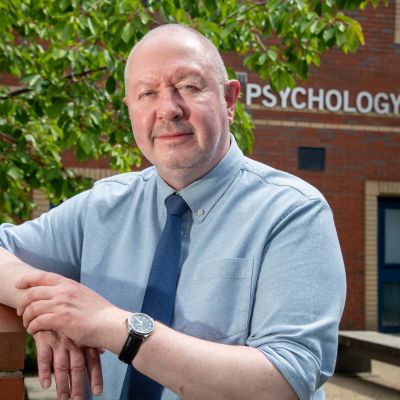 Head of School of Psychology Mitch Waterman wearing tie and leaning on a railing with Psychology sign in the background