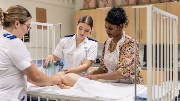 Two child nursing students work with a tutor in the clinical skills facilities
