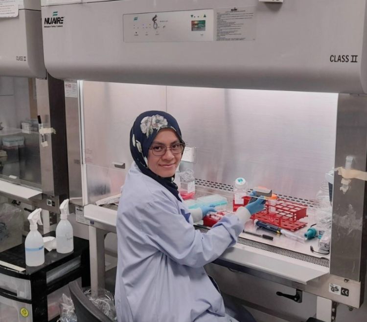 International PhD academy Medical Research student sits in a research facility and smiles at the camera.