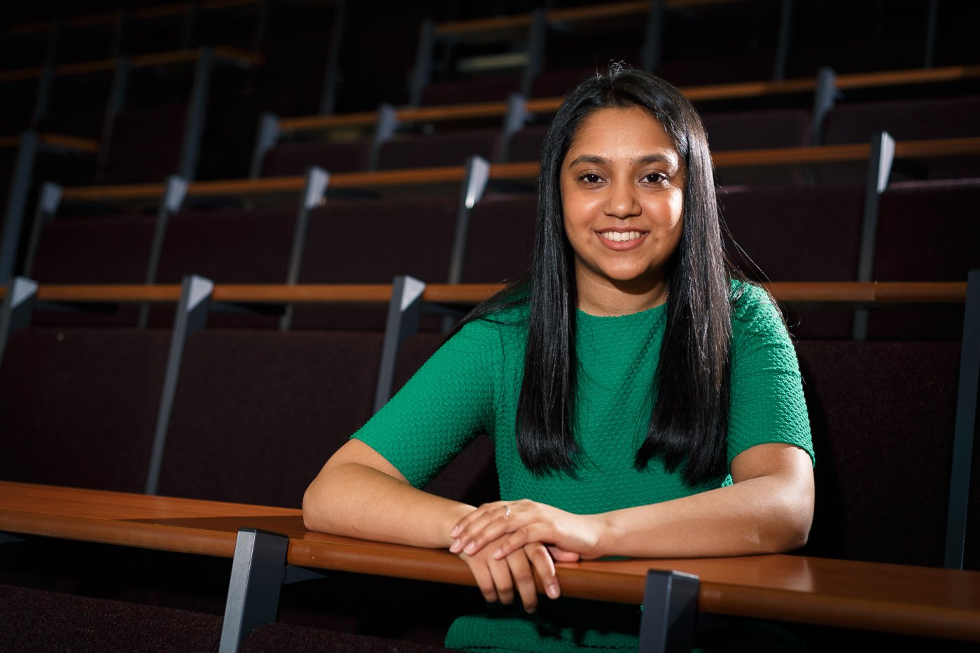 girl in a lecture theatre smiling at the camera wearing a green top