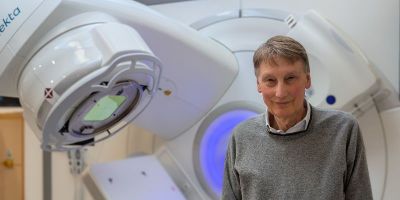 Professor Adrian Crellin CBE in front of radiotherapy equipment