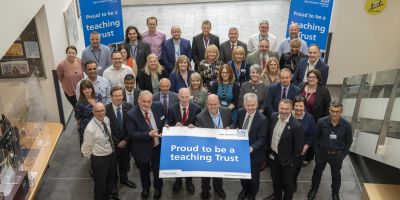 A group of colleagues at Mid Yorkshire Hospitals NHS Trust holding up a sign saying that they are proud to. be a Teaching Trust