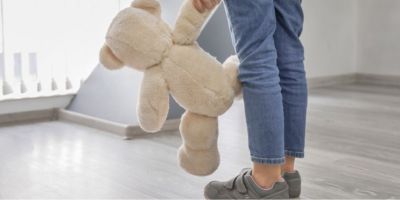 A child's legs and hand, holding a teddy bear.