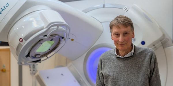 Professor Adrian Crellin CBE in front of radiotherapy equipment