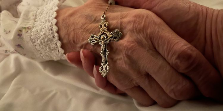 Close up of two hands holding each other, with a decorative Christian cross pendant on top of one hand