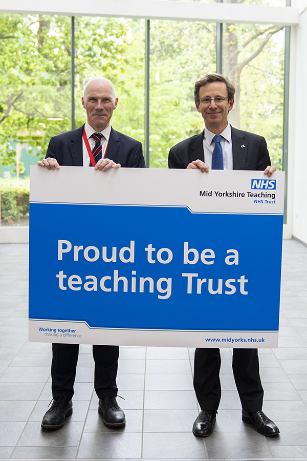 Mark Kearney and Alan Mighell holding up a sign that says 'proud to be a teaching Trust'