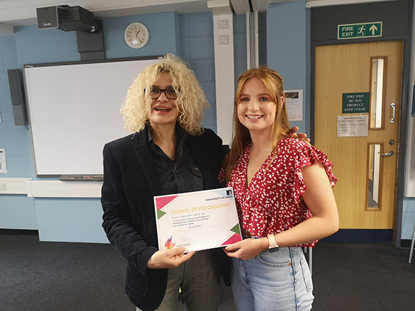 Molly Nash smiling holding her award certificate standing with Dr Gina Koutsopoulou