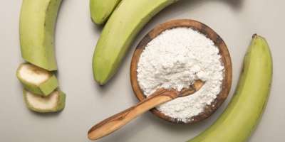 Green bananas around a bowl of flour with a wooden spoon in the flour